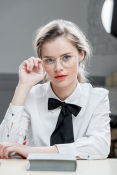 vertical portrait of a beautiful girl in stylish glasses sitting at table