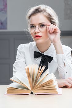 charming successful girl in glasses with a book at the table sits