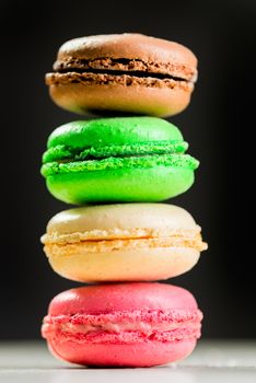 four multicolored macaroni cookies on a black background isolated