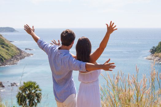 Young couple on vacation looking at sea together with hands raised