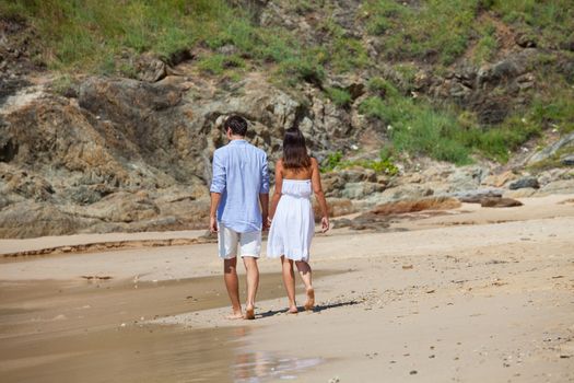 Happy couple walking on sand of tropical beach