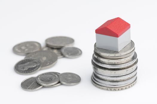 Conceptual visualization of property related financial act by means of coins with plastic miniature cottage for a white background
