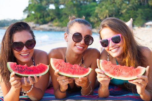 Happy smiling female friends eating watermelon on beach