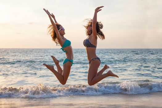 Happy female friends having fun on beach at sunset