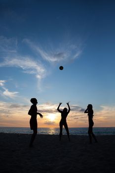 Group of young people playing volleyball on beach at sunset