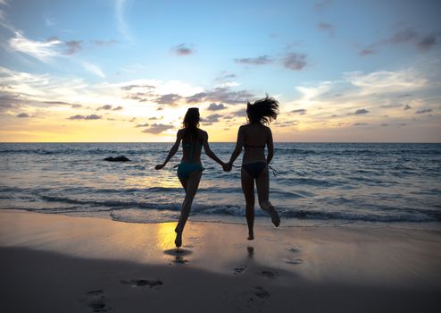 Happy female friends having fun on beach at sunset