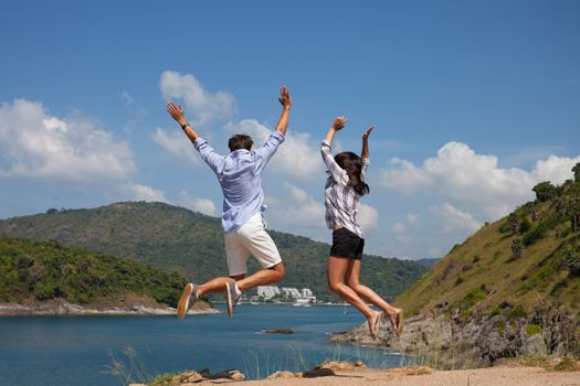 Young couple jumping, beautiful sea view on background