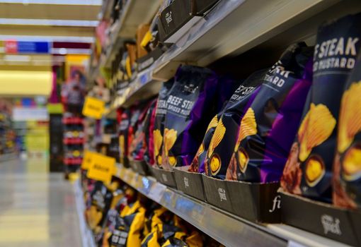 Blurred section spiced chips, spiced crisps  at retail store in Europe.  Aisle in local supermarket, defocused background.