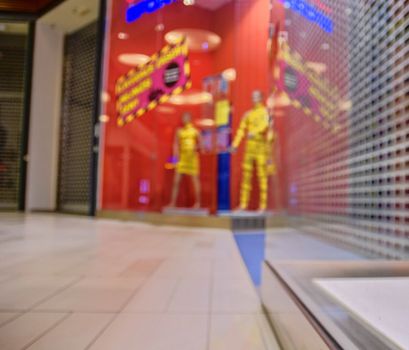 Blurred shop windows at retail store in Europe. Corridor in local supermarket, defocused background. Fashion clothes retail store sale display with female woman mannequin.