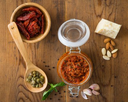 Pesto with dry tomatoes and almonds in a glass jar on a wooden table