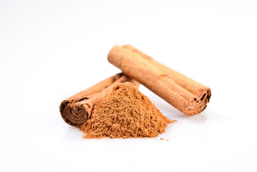 macro photograph of cinnamon sticks dry beside a teaspoon of ground cinnamon