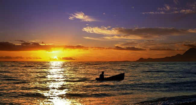Silhouette of a little fishing boat on sunset.