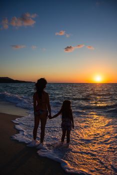 mother and daughter watching the sunset standing on the beach
