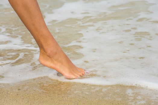 woman's foot on the beach hit by wave