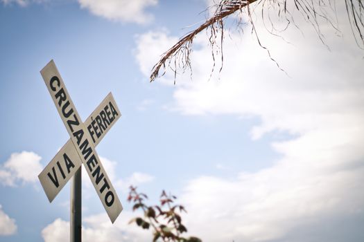 View of railroad crossing sign written in portuguese against cloudy sky