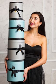 Smiling woman in black dress holds a pile of presents