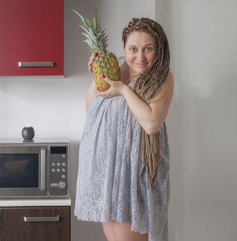 A pregnant woman with summer dress holding pineapple in the kitchen.