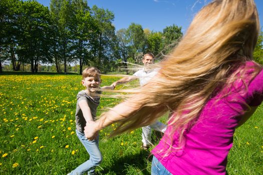 Happy family with children having fun round dancing holding hands together in city park