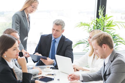 Business person group in formalwear discuss documents at meeting in modern office