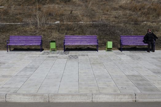 young woman sitting on a bench. next few benches. on the street early spring. on the ground paving stones.