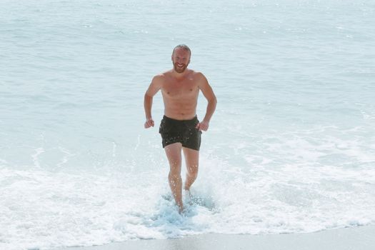 Happy smiling man with perfect body running from sea waves