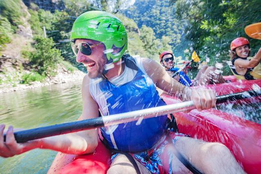 A happy laughing male in a canoe is being sprayed with water by his friends from another boat.