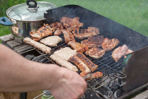 A BBQ with meat and wooden charcoal smokes outdoors.