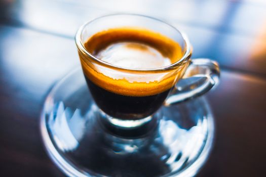 Espresso coffee in glass cup on wooden table, colorful reflections and shallow depth of field.