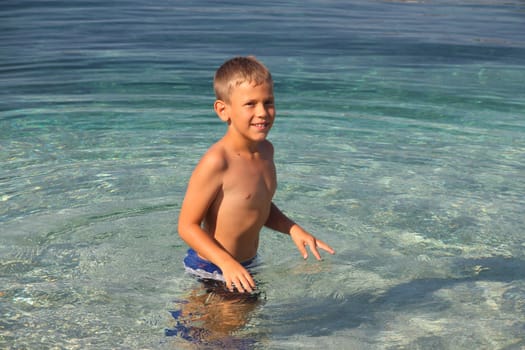 Happy little boy smiling standing in clear transparent sea water