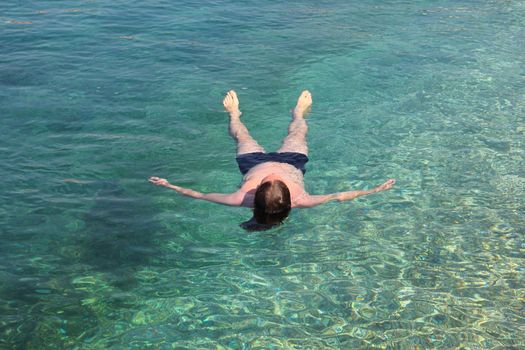 Vacation and relaxation concept, man floating relaxed on back in transparent pure blue sea water