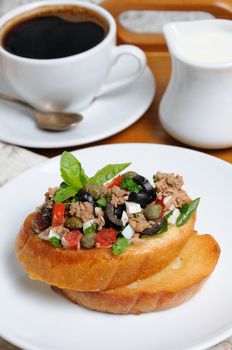 Breakfast from fried toast with chopped tuna with egg, cubes of tomatoes and olive slices, capers with a cup of coffee, a coffee pot on a tray