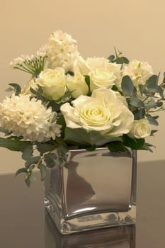 White wedding bouquet of flowers including roses, white lilac, hydrangea, star of David and hyacinth in a reflective mirror vase.
