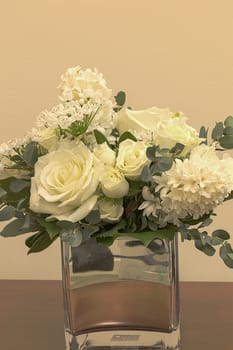 White wedding bouquet of flowers including roses, white lilac, hydrangea, star of David and hyacinth in a reflective mirror vase.