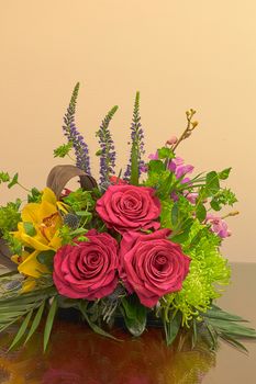 Pink roses, yellow cymbidium , green mums, and palms in a tropical bouquet floral arrangement on a reflective surface