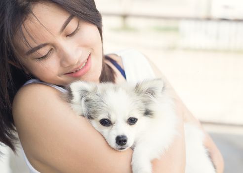 Closeup happy woman with white pomeranian dog on hand, pet health care concept with soft and selective focus