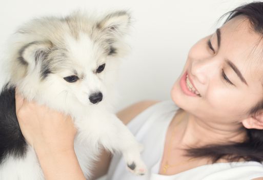 Closeup happy woman with white pomeranian dog on hand, pet health care concept with soft and selective focus