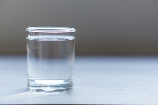 Glass of water on wood table with light in the morning, healthy care concept, selective focus