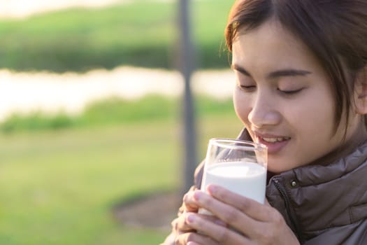 Closeup woman drinking milk with happy face and green nature background, selective focus, healthy care concept