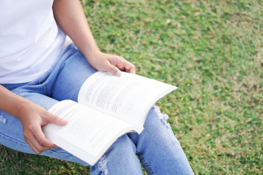 Closeup young woman reading a book sitting on green grass with relax feelling