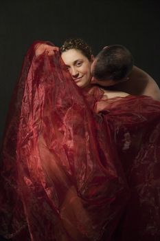 Happy pregnant woman covered with red veil is being kissed by a male.