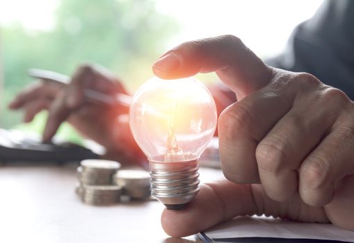 Hand holding light bulbs glowing and using calculator. Idea, creativity and saving energy with light bulbs concept.