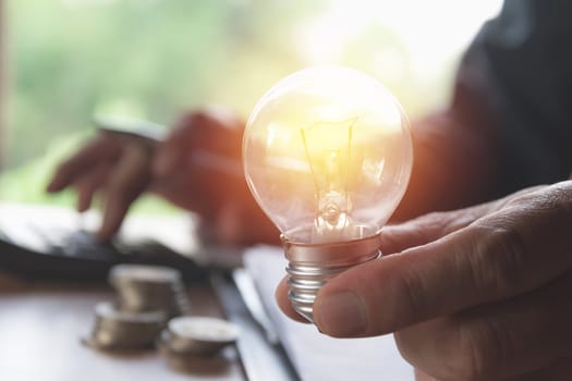 Hand holding light bulbs glowing and using calculator. Idea, creativity and saving energy with light bulbs concept.