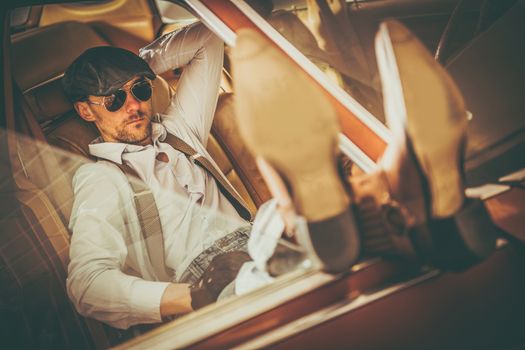 Caucasian Men in His 30s Western Wearing and Sunglasses Enjoying the Moment and in His American Classic Car Keeping His Legs on the Vehicle Door. 