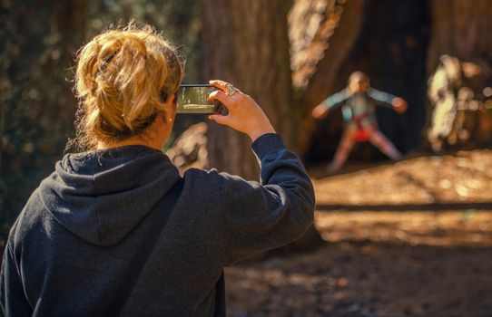 Taking Family Photos and Videos Using Smartphone. Caucasian Woman in Her 30s Talking Photo of Her Daughter While Exploring Sequoia National Park.