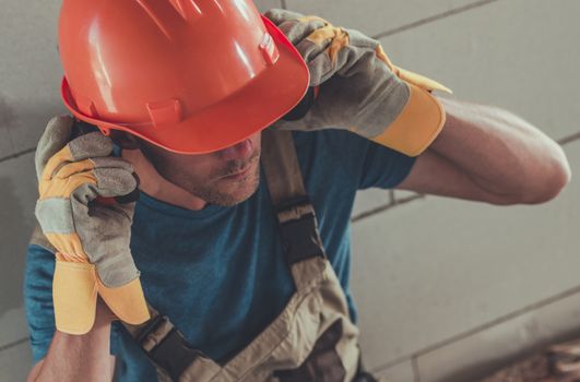 Professional Construction Protection Equipment. Caucasian Contractor Wearing Noise Reduction Headphones, Hard Hat and Protection Gloves.