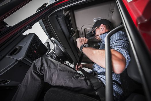 Caucasian Truck Driver Using Seat Belts For his Safety. Heavy transportation Safety.