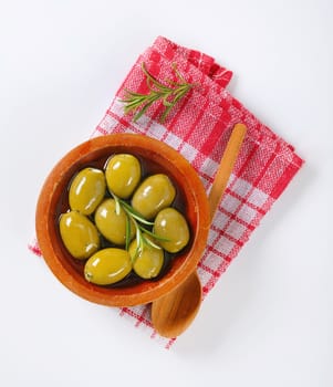 bowl of green olives with rosemary and wooden spoon on checkered dishtowel