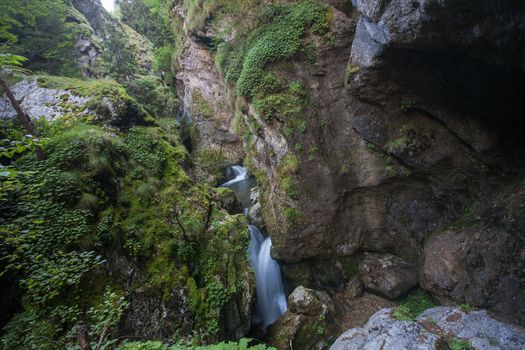 A natural waterfall between beautiful rocks covered with green moss.