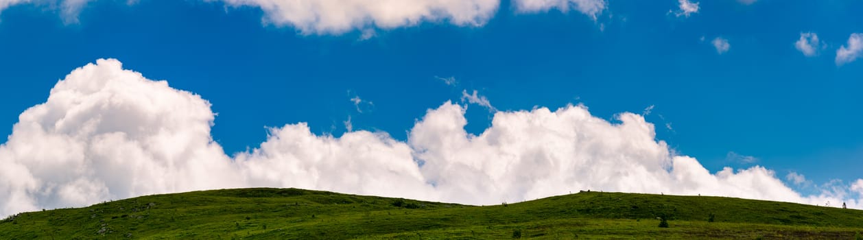 cloud rising behind the grassy hills. lovely panorama of cloudscape on a blue sky