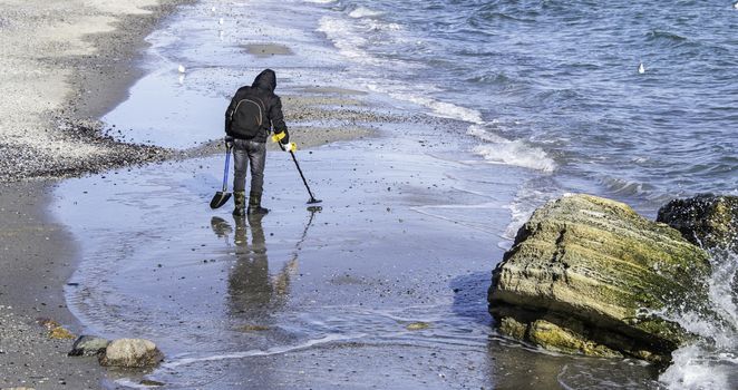 ODESSA, UKRAINE - 01.25.2017. Man with metal detector looking for treasure on the beach in a early winter morning.